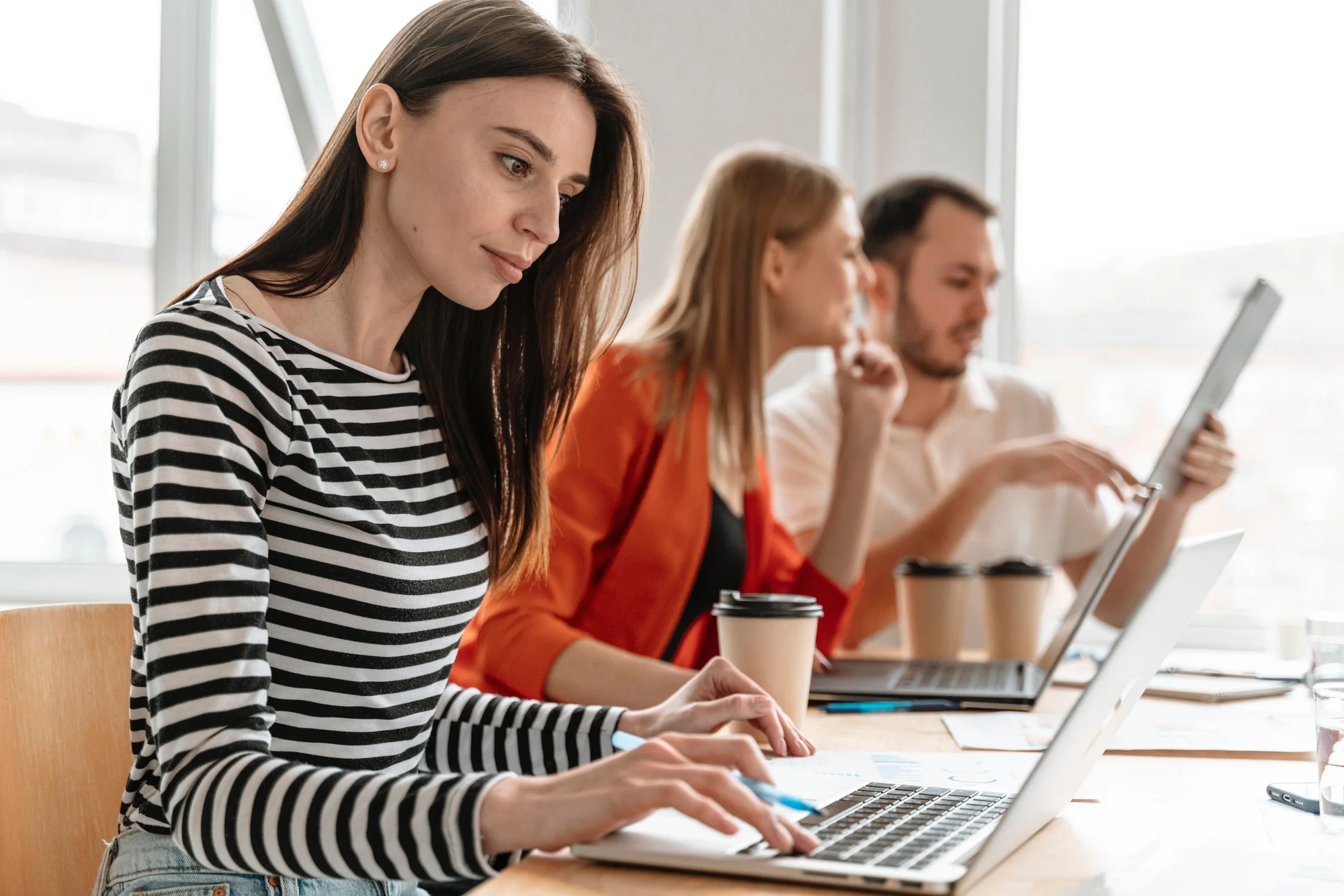 Collaboratrice travaillant sur ordinateur pendant qu'une équipe échange autour d'un projet digital